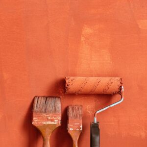 Close-up of paintbrushes and roller with orange backdrop, perfect for home renovation concepts.